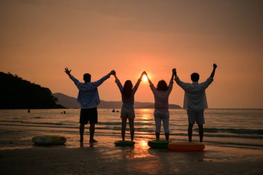 Gün batımında kumsalda el ele tutuşan mutlu aile manzarası. Birlikte huzurlu deniz kenarındaki anın tadını çıkarıyoruz. Birlik, sevgi ve aile yaşam tarzının sembolü.
