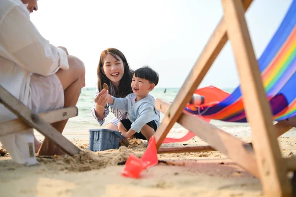 Tatilde, ebeveynler plaj sandalyelerinde oturup, gün boyunca çocuklarının kumsalda kum oyuncaklarıyla oynamasını seyrederler.