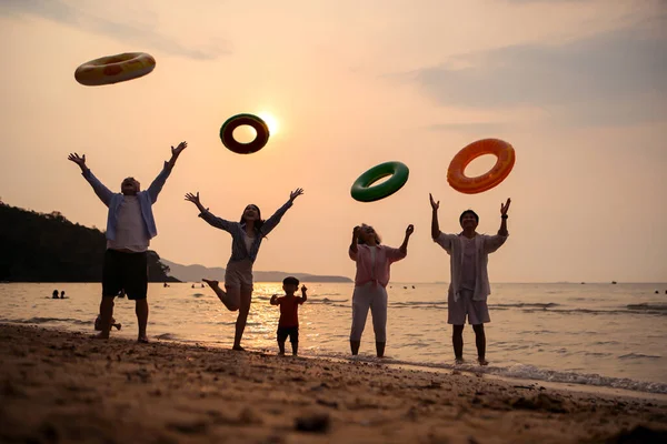 Mutlu çoklu nesil aile gün batımının tadını çıkarıyor. Renkli şişme yüzme yüzükleri atıyor. Deniz kenarında özgürlük, neşe ve yaz yaşam tarzını ifade ediyor.