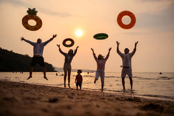 Mutlu çoklu nesil aile gün batımının tadını çıkarıyor. Renkli şişme yüzme yüzükleri atıyor. Deniz kenarında özgürlük, neşe ve yaz yaşam tarzını ifade ediyor.