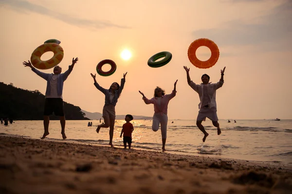 Mutlu çoklu nesil aile gün batımının tadını çıkarıyor. Renkli şişme yüzme yüzükleri atıyor. Deniz kenarında özgürlük, neşe ve yaz yaşam tarzını ifade ediyor.