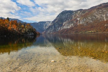 Slovenya 'daki Bohinj Gölü' nün güzel sonbahar manzarası, canlı renkler, durgun su ve etkileyici dağlarla. Huzurlu ve büyüleyici bir sahne.