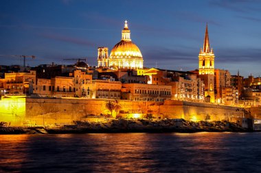 Valletta, Malta 'nın akşam manzarası, Carmel Dağı Kubbesi ve St. Paul' s Anglikan Katedrali 'nin koyu mavi alacakaranlık gökyüzüne karşı sıcak aydınlatan Bazilikası sergileniyor..