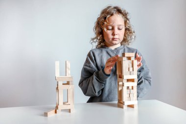 Kıvırcık saçlı çocuk ahşap yapı taşlarıyla oynuyor, uzun bir kule yaratmak için parçaları dikkatlice istifliyor. Yaratıcılık, odaklanma ve erken çocukluk gelişimi kavramı. 