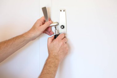 Erkek eller, kapı kolu ve kilit mekanizmasını tamir etmek için tornavida kullanıyor. Ev bakımı ve pratik DIY becerileri sergiliyor..