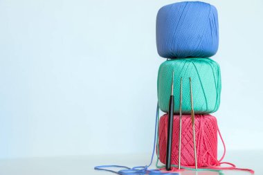 Dikey olarak dizilmiş renkli iplikçikler ve hafif pastel arka planda onlara yaslanmış kancalar. Örgü, tığ işi, el işi, DIY projesi, tekstil tasarımı ve yaratıcı hobiler için minimalist kompozisyon.
