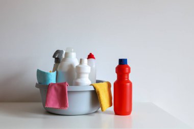 Plastik bir leğende temizlik malzemeleri: deterjan şişeleri, sprey, lastik eldivenler ve beyaz arka planda mikrofiber bezler. Ev temizliği, dezenfeksiyon ve hijyenik ev işleri kavramı.