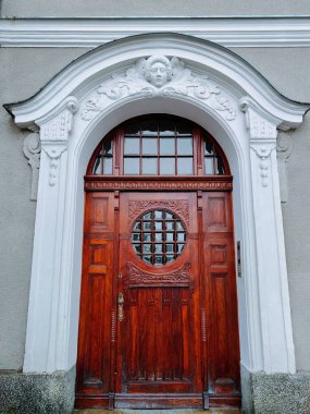 Süslü ahşap giriş kapısı yuvarlak pencere ve oymalı detaylar, heykeltraş yüzüyle beyaz kaplama, tarihi bina cephesi, ön görünüş, mimari miras ve tasarım konsepti, insan yok.
