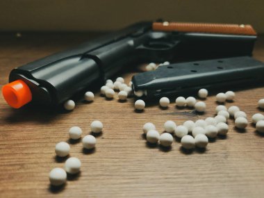 Üzerinde turuncu detaylar ve beyaz plastik toplarla çevrili bir şarjör olan siyah bir oyuncak tabanca. Sahne eğlenceli ve maceralı bir atmosferi çağrıştırıyor. Oyunların tipik çekimi..