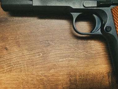 Tahta bir masanın üzerinde duran yarı otomatik bir tabancanın yakın çekimi. Tetikleyicinin detaylarına ve silahın bitimine odaklanacağız..