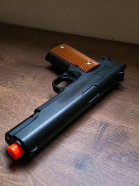 Metalik detayları ve yapay tahta sapı olan oyuncak bir silah. Hem güzelliği hem de tehlikeyi somutlaştıran yumuşak bir kopya..