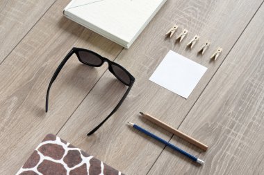 Beyaz ve benekli kitaplar, çıkartma, kurşun kalem, mandal ve güneş gözlüğü bileşimi. Nesneleri güzel parke zemin koydu.