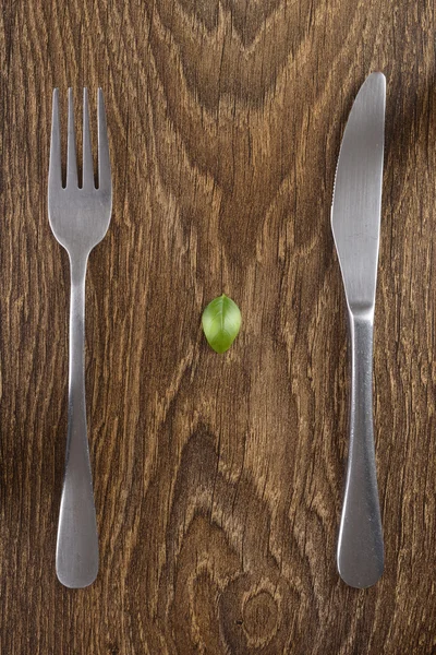 Μαχαιροπίρουνα σε ένα σκοτεινό ξύλινο τραπέζι. Φύλλα βασιλικού. — Φωτογραφία Αρχείου