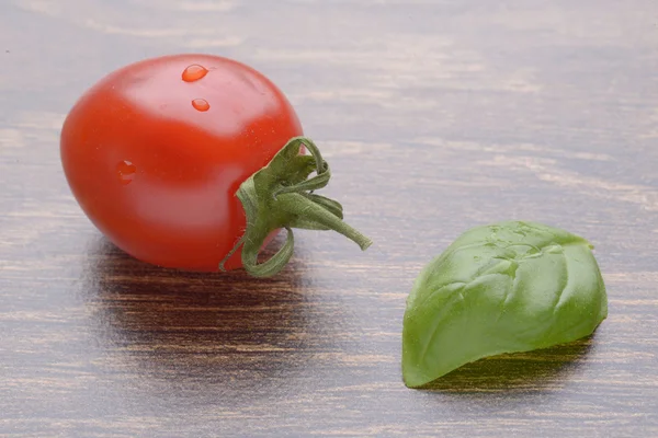 Tomates cherry en una mesa oscura. Un montón de gotas de agua. Hoja de albahaca . — Foto de Stock