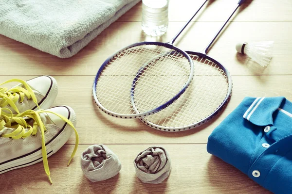 Rackets zorgen voor een badminton shuttle, polo shirts, schoenen, handdoek en water op een houten vloer. Retro effect, — Stockfoto