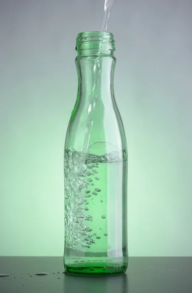 Green bottle with clean drinking water on the table. Bubbles in the glass transparent bottle.
