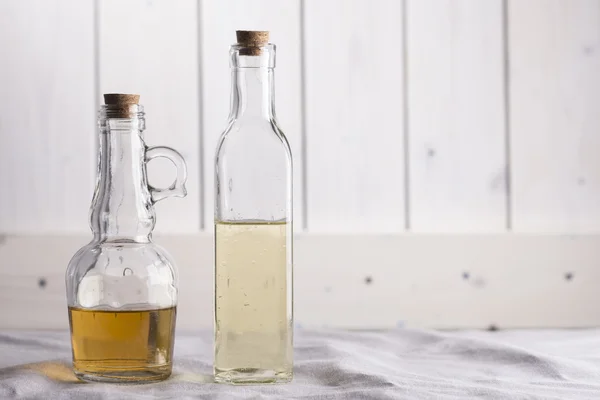 Frascos transparentes con aceite y vinagre sobre fondo de madera blanca . —  Fotos de Stock