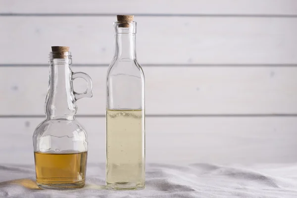 Frascos transparentes con aceite y vinagre sobre fondo de madera blanca . — Foto de Stock