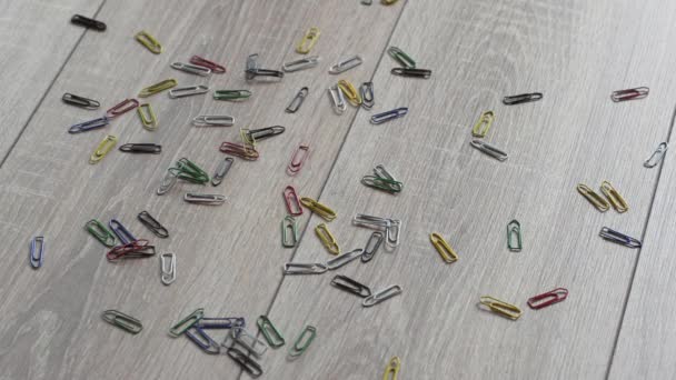 Paperclip spilled on a beautiful wooden floor. Falling small colored paperclip backlit. Reverse. — Stock Video