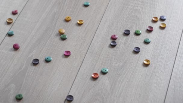 Colored buttons spilled on a beautiful wooden floor. Falling buttons backlit. Reverse. — Stock Video