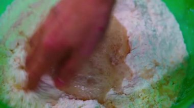 Close-up of a person using a hand to mix flour and liquid in a bowl, preparing dough for home baking. High quality 4k footage
