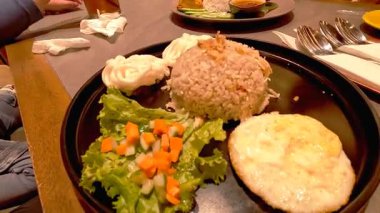 Kızarmış yumurta, turşu ve krakerle servis edilen tavuklu bir tabak Endonezya pilavı.