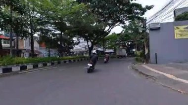 5 Nisan 2025 'te, Bandung, Batı Java, Endonezya' daki iş yerlerine giderken, güneşli bir kavşakta motosiklet ve araba sürenlerin 4K kaydı.
