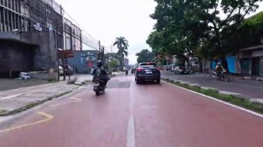 5 Nisan 2025 'te, Bandung, Batı Java, Endonezya' daki iş yerlerine giderken, güneşli bir kavşakta motosiklet ve araba sürenlerin 4K kaydı.