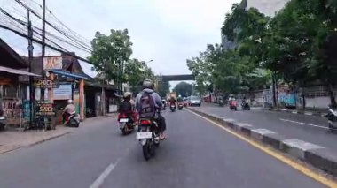 5 Nisan 2025 'te, Bandung, Batı Java, Endonezya' daki iş yerlerine giderken, güneşli bir kavşakta motosiklet ve araba sürenlerin 4K kaydı.