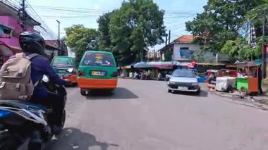 5 Nisan 2025 'te, Bandung, Batı Java, Endonezya' daki iş yerlerine giderken, güneşli bir kavşakta motosiklet ve araba sürenlerin 4K kaydı.