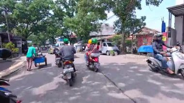 5 Nisan 2025 'te, Bandung, Batı Java, Endonezya' daki iş yerlerine giderken, güneşli bir kavşakta motosiklet ve araba sürenlerin 4K kaydı.