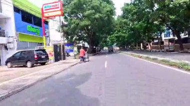 5 Nisan 2025 'te, Bandung, Batı Java, Endonezya' daki iş yerlerine giderken, güneşli bir kavşakta motosiklet ve araba sürenlerin 4K kaydı.