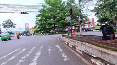 5 Nisan 2025 'te, Bandung, Batı Java, Endonezya' daki iş yerlerine giderken, güneşli bir kavşakta motosiklet ve araba sürenlerin 4K kaydı.