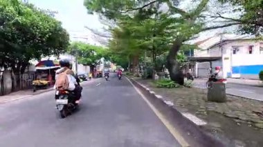 5 Nisan 2025 'te, Bandung, Batı Java, Endonezya' daki iş yerlerine giderken, güneşli bir kavşakta motosiklet ve araba sürenlerin 4K kaydı.