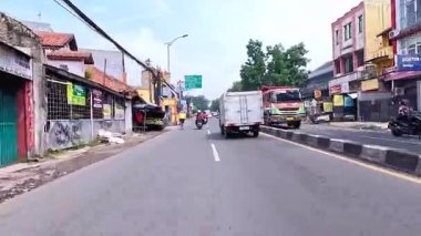 5 Nisan 2025 'te, Bandung, Batı Java, Endonezya' daki iş yerlerine giderken, güneşli bir kavşakta motosiklet ve araba sürenlerin 4K kaydı.