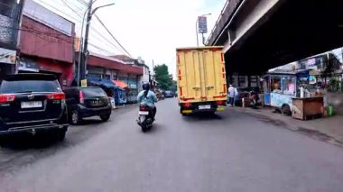 5 Nisan 2025 'te, Bandung, Batı Java, Endonezya' daki iş yerlerine giderken, güneşli bir kavşakta motosiklet ve araba sürenlerin 4K kaydı.