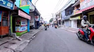 5 Nisan 2025 'te, Bandung, Batı Java, Endonezya' daki iş yerlerine giderken, güneşli bir kavşakta motosiklet ve araba sürenlerin 4K kaydı.
