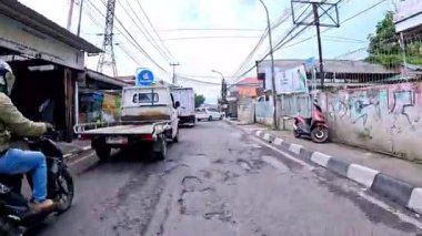 5 Nisan 2025 'te, Bandung, Batı Java, Endonezya' daki iş yerlerine giderken, güneşli bir kavşakta motosiklet ve araba sürenlerin 4K kaydı.