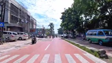 5 Nisan 2025 'te, Bandung, Batı Java, Endonezya' daki iş yerlerine giderken, güneşli bir kavşakta motosiklet ve araba sürenlerin 4K kaydı.