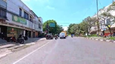 5 Nisan 2025 'te, Bandung, Batı Java, Endonezya' daki iş yerlerine giderken, güneşli bir kavşakta motosiklet ve araba sürenlerin 4K kaydı.