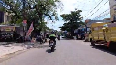 5 Nisan 2025 'te, Bandung, Batı Java, Endonezya' daki iş yerlerine giderken, güneşli bir kavşakta motosiklet ve araba sürenlerin 4K kaydı.