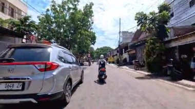 5 Nisan 2025 'te, Bandung, Batı Java, Endonezya' daki iş yerlerine giderken, güneşli bir kavşakta motosiklet ve araba sürenlerin 4K kaydı.