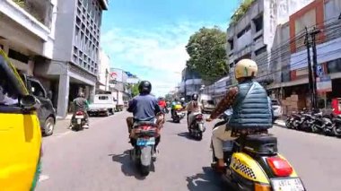 5 Nisan 2025 'te, Bandung, Batı Java, Endonezya' daki iş yerlerine giderken, güneşli bir kavşakta motosiklet ve araba sürenlerin 4K kaydı.