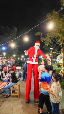 İnsanlar Bandung 'da 23 Aralık 2025' te Noel Baba kılığındaki bir stilt yürüyüşçüyle yapılan bir gece etkinliğinin keyfini çıkarıyorlar..