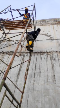 İnşaat alanında beton duvarlı güvenlik donanımı ve sarı çizme giyen işçilerin detaylı fotoğrafı. Bandung 20 Mayıs 2025