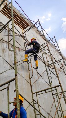 İnşaat alanında beton duvarlı güvenlik donanımı ve sarı çizme giyen işçilerin detaylı fotoğrafı. Bandung 20 Mayıs 2025