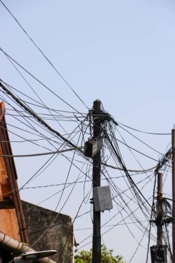 Endonezya 'nın bir kentsel bölgesindeki iki elektrik direğindeki karmaşık elektrik kablolarının ve telekomünikasyon kablolarının fotoğrafı.