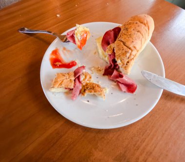 Kahvaltı için iştah açıcı sosisli sandviçin yakın plan fotoğrafı. Kahvehanedeki ahşap masada çatal ve bıçakla servis ediliyor..