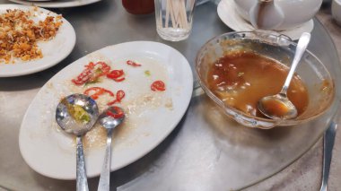 Dağınık tabakta arta kalan yemekler ve bir kaşıkla cam kasede, restoranda bitirilmiş bir yemek olduğunu gösteriyor..