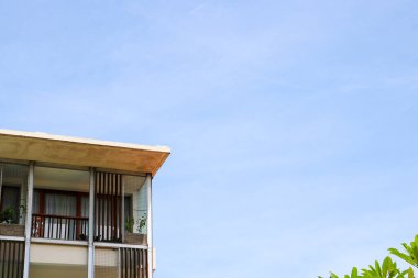 Tropikal ev tasarımı, parlak mavi gökyüzüne karşı dikey kereste levhaları ile ikinci katın balkonunu gösteriyor..
